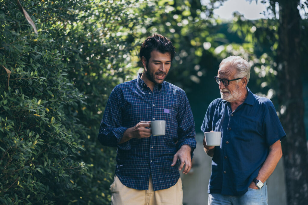 Father and son outside house, enjoying a stress-free cup of coffee.