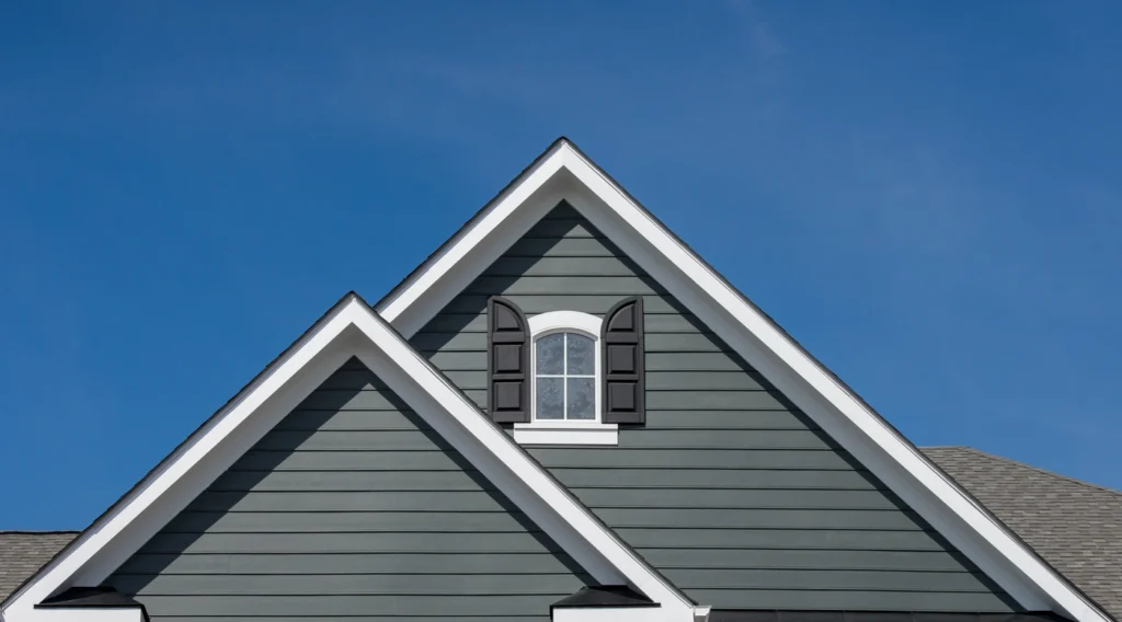 A grey house with vinyl siding colors features a triangular roof and white trim