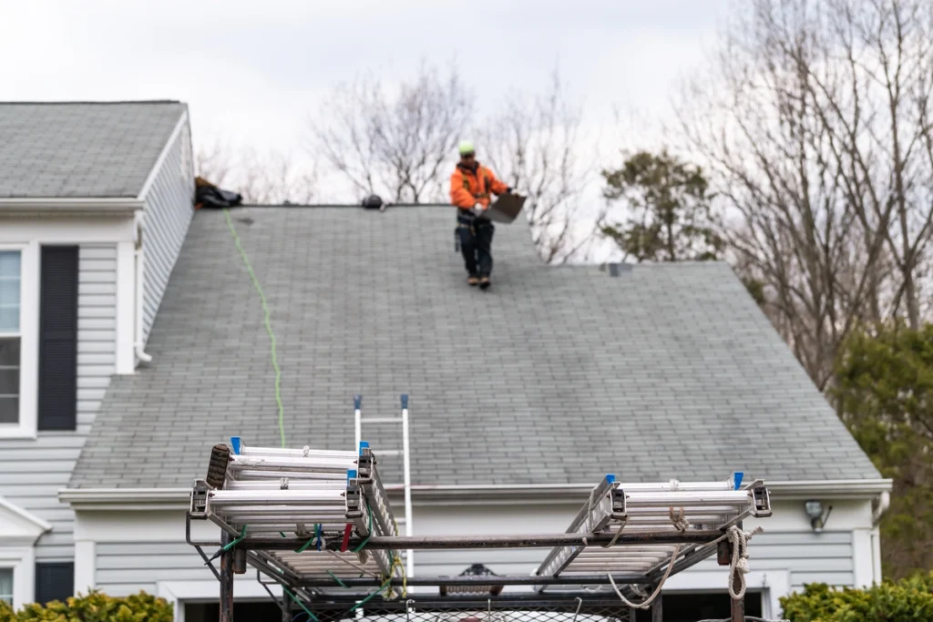 Roofing contractor inspects rooftop using ladder and safety equipment