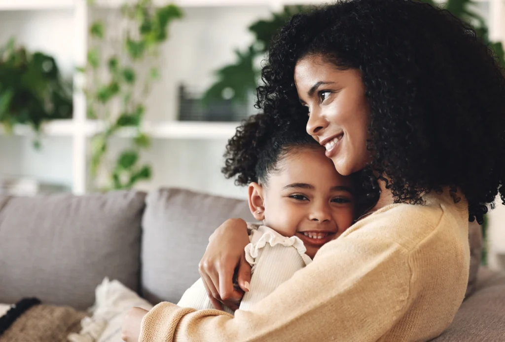 Mom and young daughter hug on couch in king of prussia home