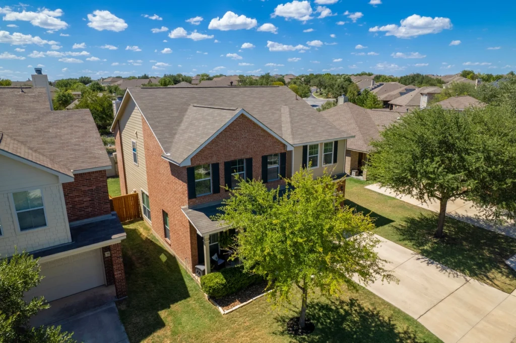 An aerial view of a suburban neighborhood showcases a charming two-story brick house with large windows and a well-maintained lawn. Surrounded by trees and adjacent homes, this picturesque scene unfolds under a bright blue sky—perfectly illustrating the superior craftsmanship of roofing services in Horsham.