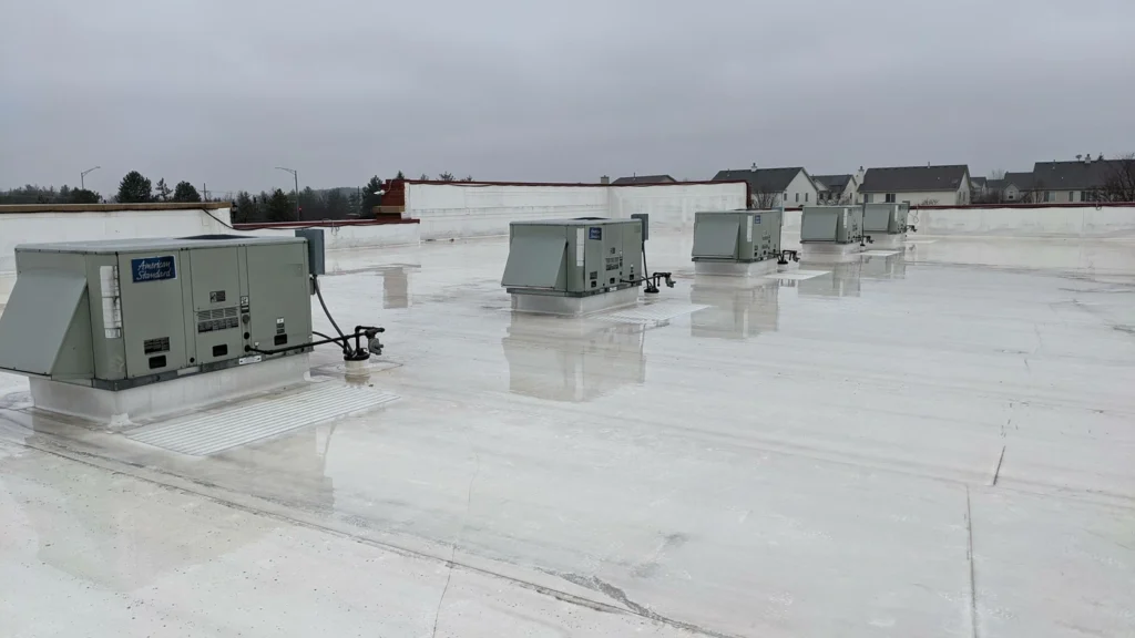 A flat, white commercial rooftop on a cloudy day with multiple large HVAC units evenly spaced. The rooftop is wet, reflecting the overcast sky
