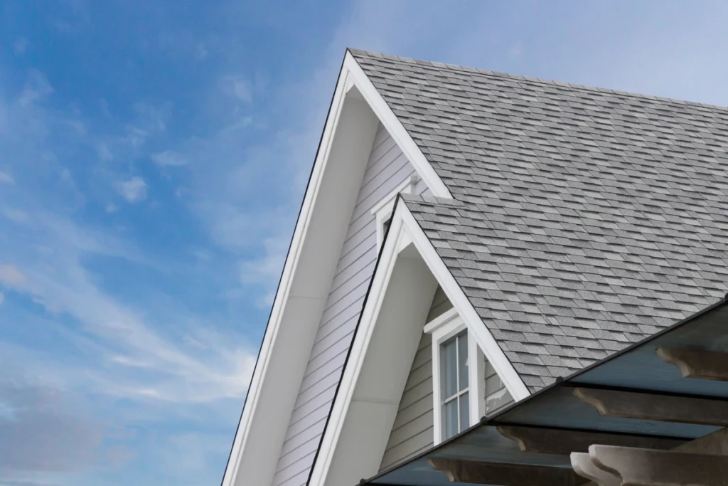 Close-up of a residential house roof with gray shingles and white trim, set against a blue sky with a few clouds. The roofing team in Broomall crafted the building's steep gable design flawlessly.
