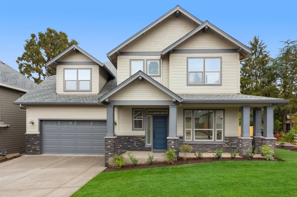 A modern two-story house with light gray siding and dark gray Berwyn roofing accents. It features multiple gabled roofs, large windows, and a two-car garage. The front yard is landscaped with a small lawn and shrubs.
