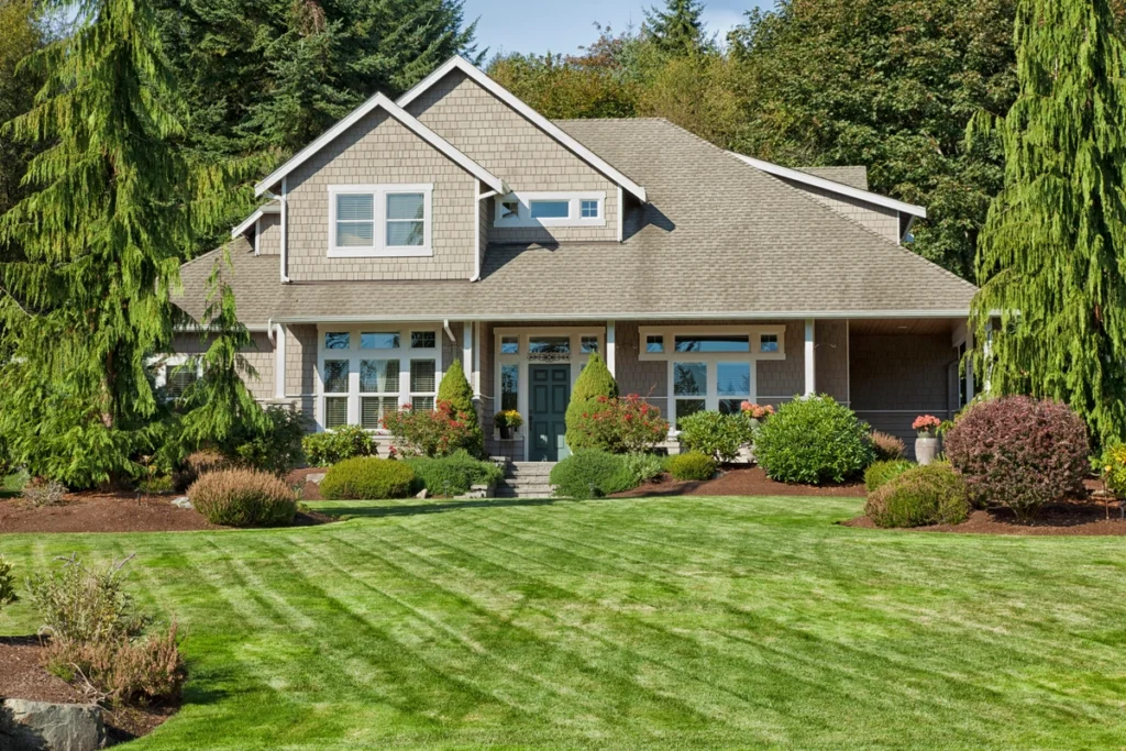 A charming two-story house in Royersford boasts a gabled roof, surrounded by lush green landscaping, including neatly trimmed bushes and tall trees. The front yard features a well-maintained grassy lawn, and there are colorful flowers near the entrance.