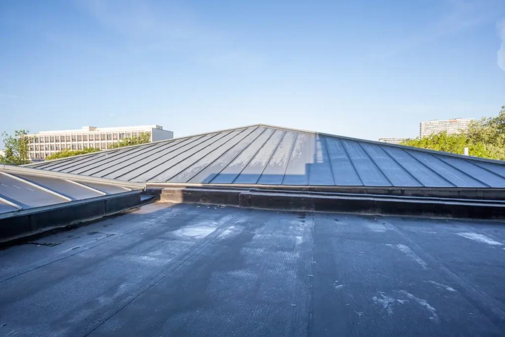 A flat rooftop covered with black rubber waterproofing membrane under a clear blue sky. In the background, a few trees and buildings are visible.