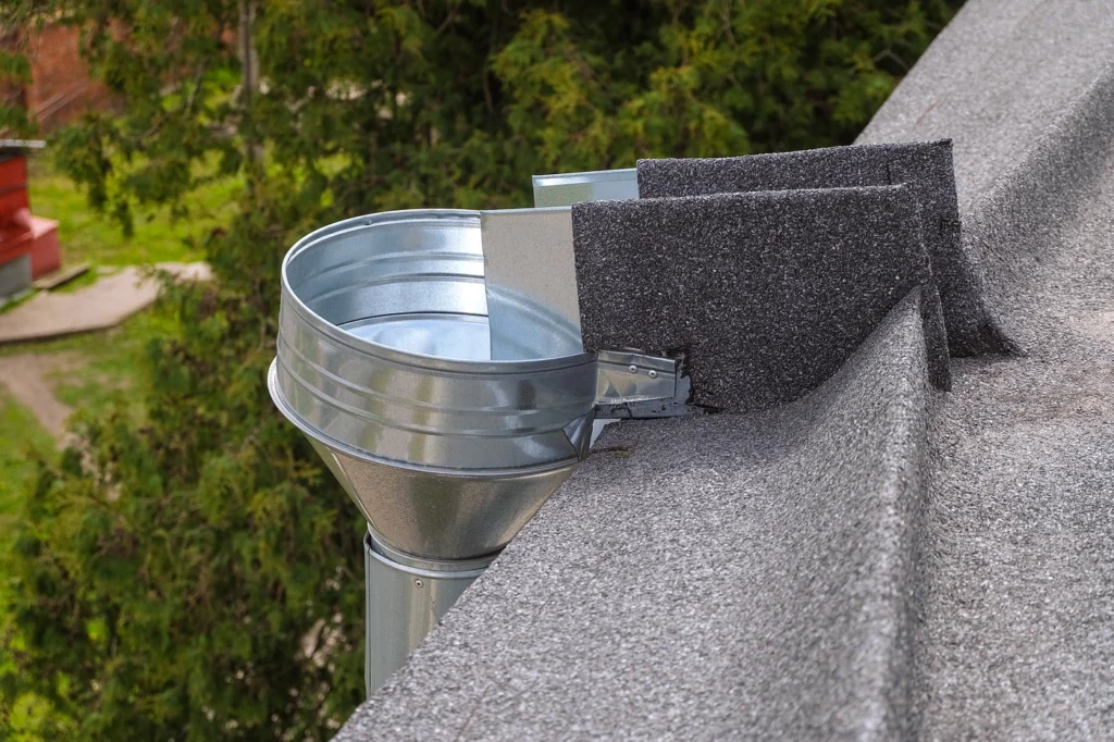 A metal rainwater gutter and downspout system graces a gray flat roofing system