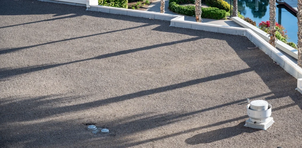 A flat gravel-covered rooftop with a close up view of roof scupper gutter drainage system