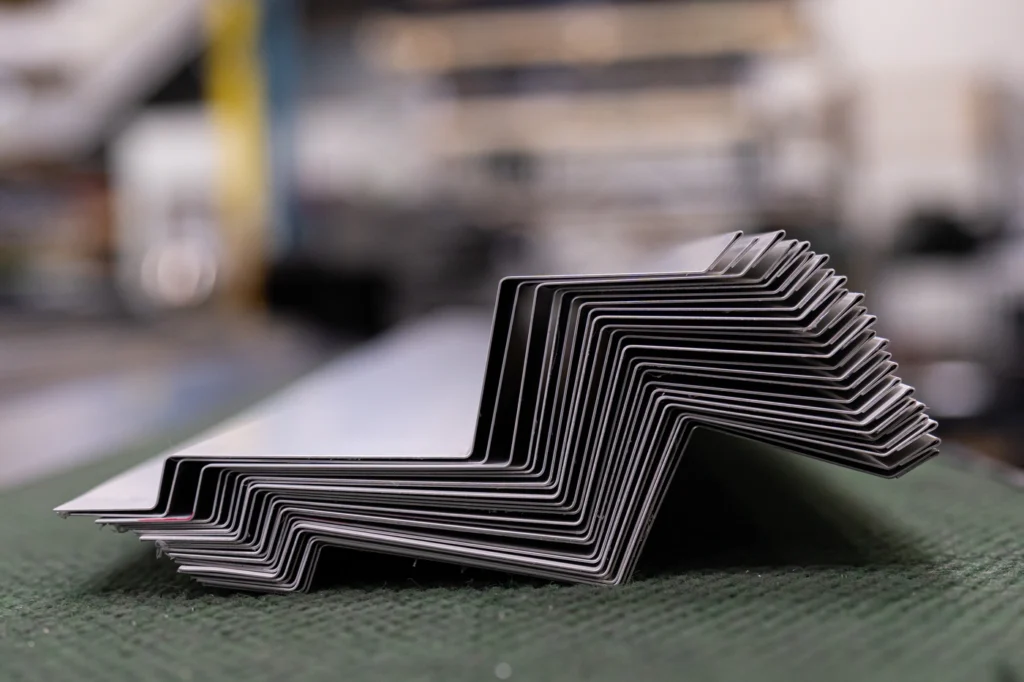 Stack of bent metal sheets, likely used for flat roof flashing, arranged in a zigzag pattern and photographed close-up on a green surface with a blurred industrial background