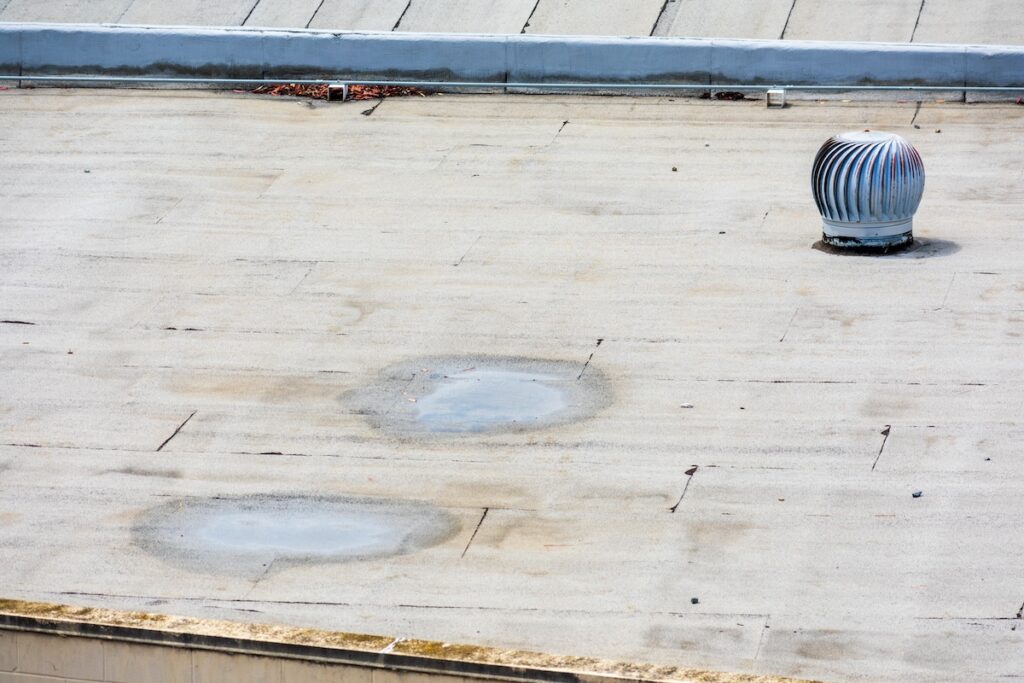 A flat rooftop with a silver rotating ventilator on the right. The surface shows two large circular stains and some scattered debris along one side.