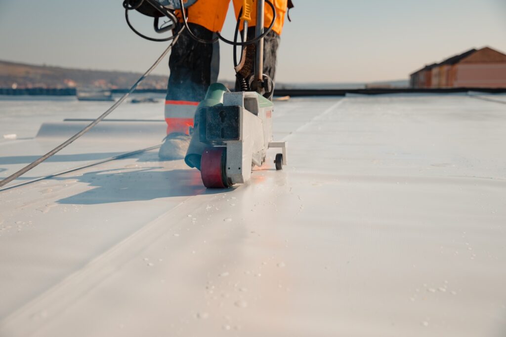 Worker in safety gear uses a machine to seal a white, flat roof