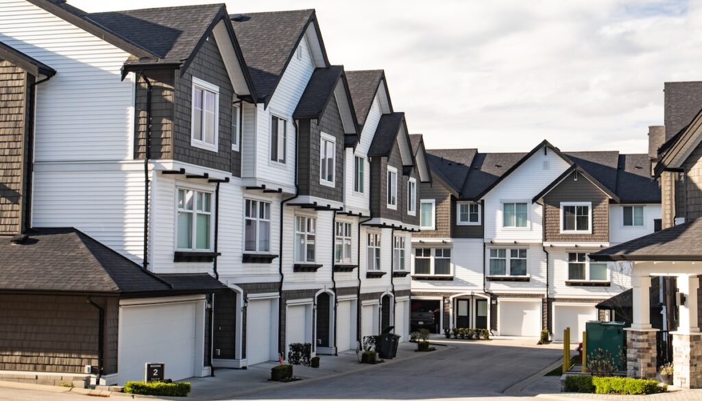 A row of modern townhouse units with multiple stories, featuring gray and white siding, gabled roofs, and large windows