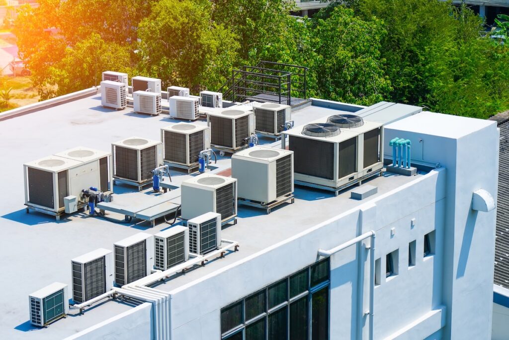 Rooftop view of multiple air conditioning units on a white building.