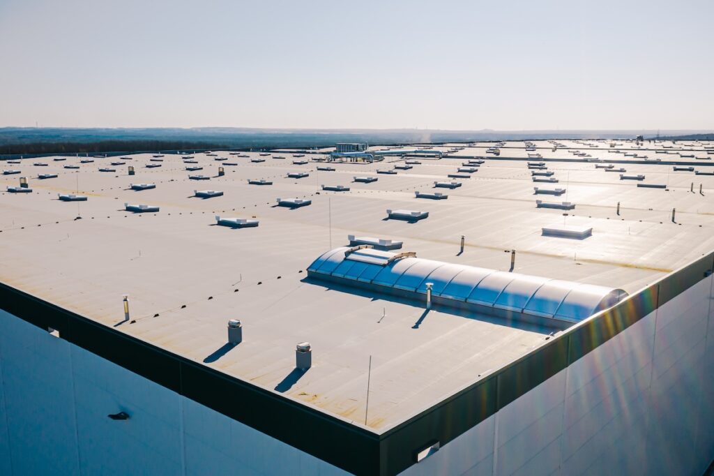 Aerial view of a large, flat industrial rooftop with numerous ventilation units and skylights. 