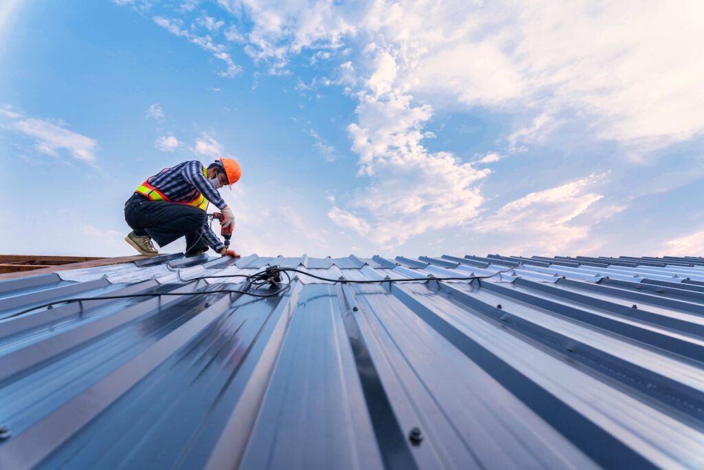 Worker in a hard hat and safety vest installing or inspecting a metal roof