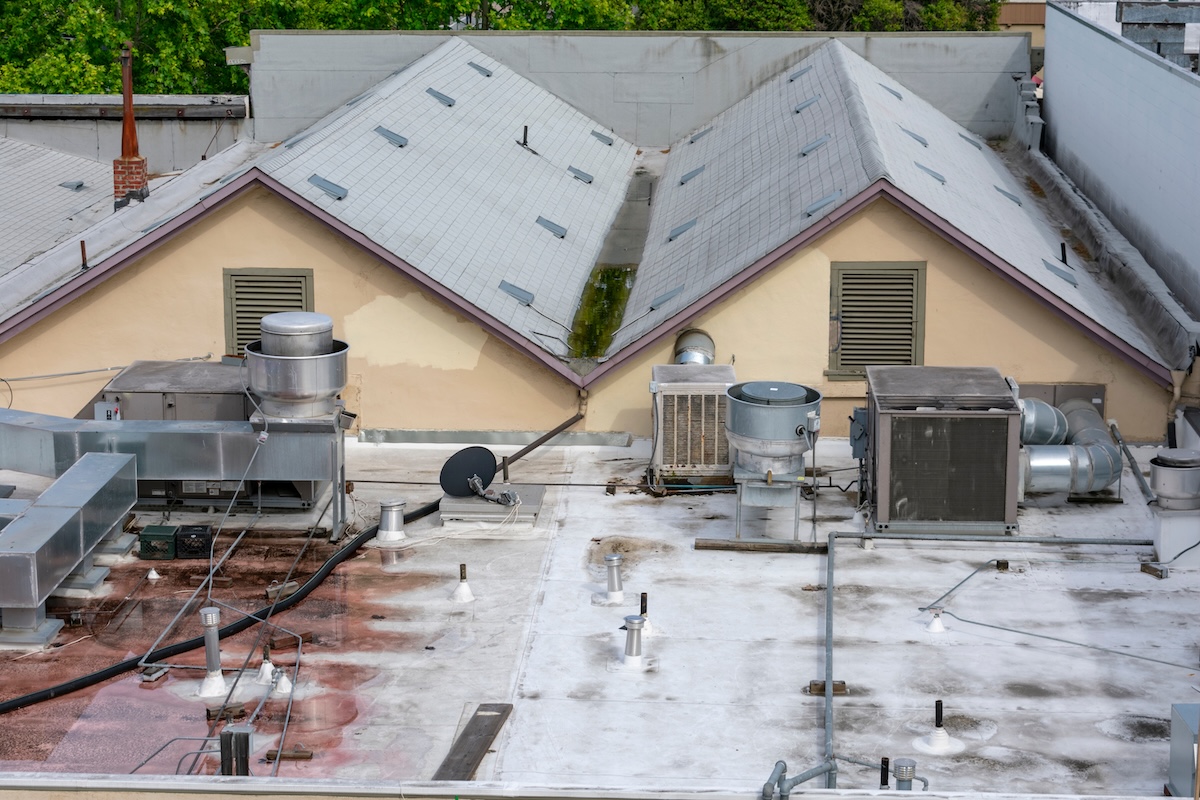 A flat rooftop with multiple HVAC units, vents, pipes, and equipment. With water pooling on roof