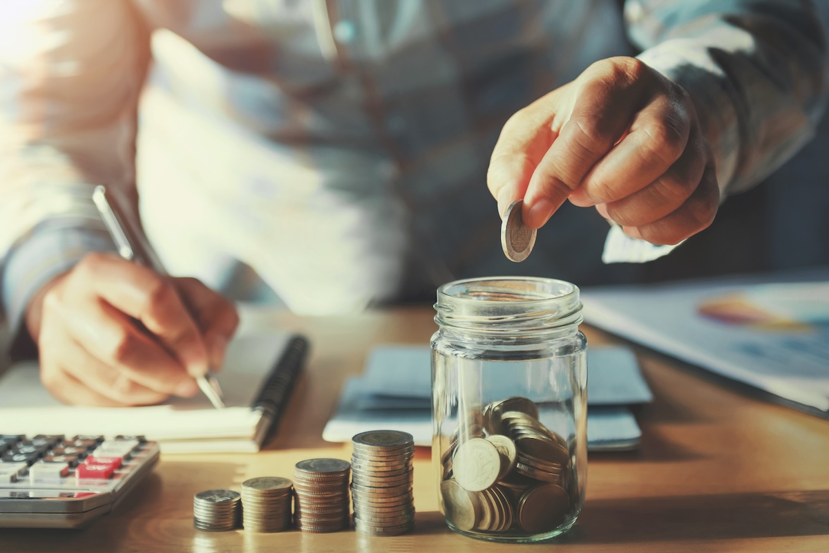 A person places a coin into a glass jar filled with coins