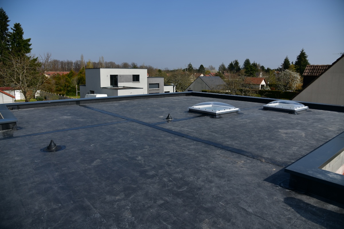 Flat rooftop of a modern building with a black EPDM roof membrane, two dome-shaped skylights, and small vents