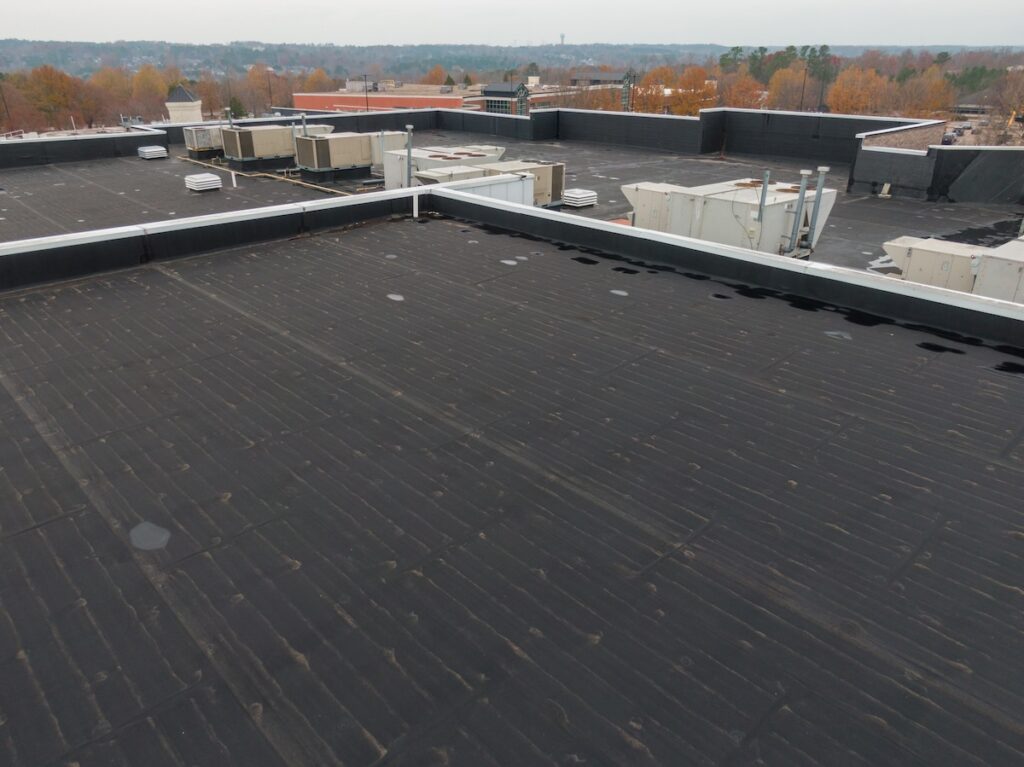 A large flat black EPDM roof with several HVAC units and vents, surrounded by low walls.