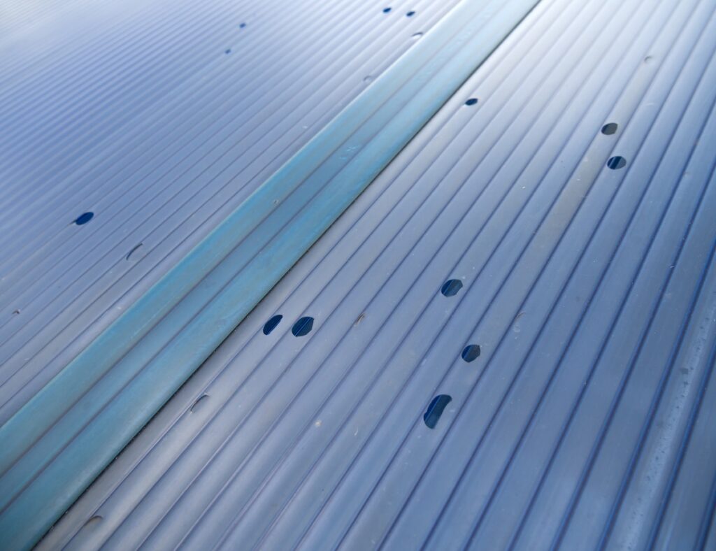 Close-up of a corrugated metal surface with small holes and dents from flat roof hail damage