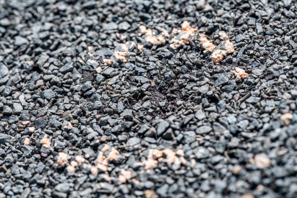 Close-up of a rough, black gravel surface showing flat roof hail damage