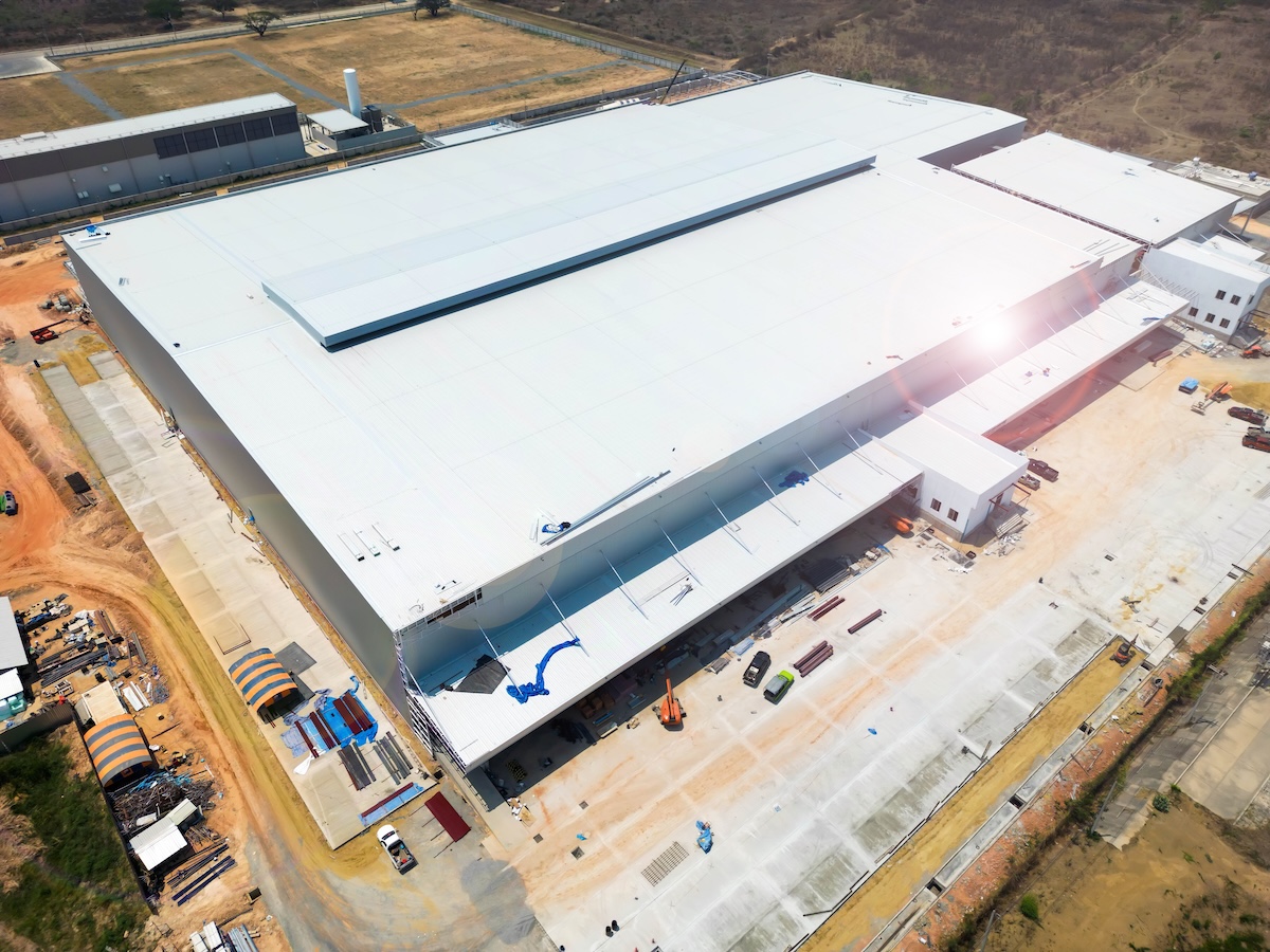 Aerial view of a large, white industrial warehouse with a flat roof to pitched roof transition
