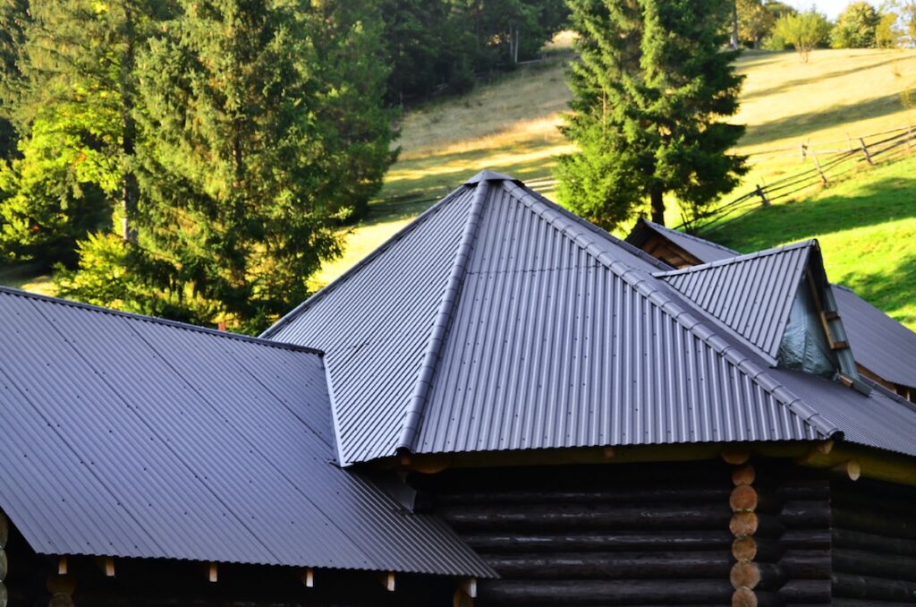 The roof is made of gray embossed metal sheets. Wooden house in the summer field