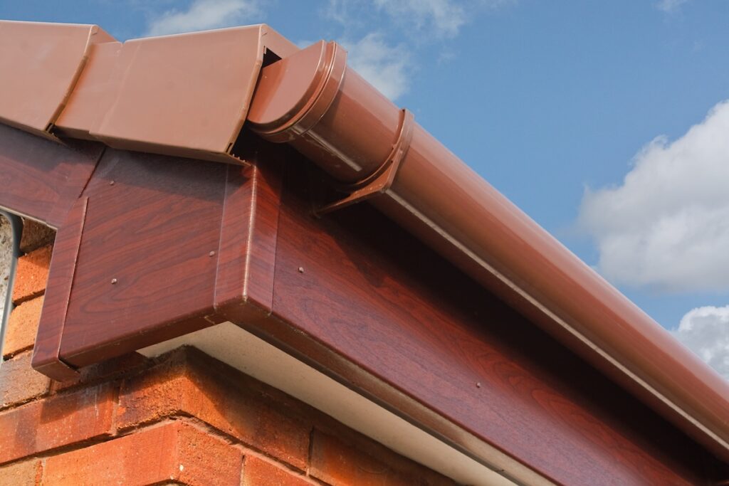 Close-up of a house roof corner showing brown plastic gutters and fascia
