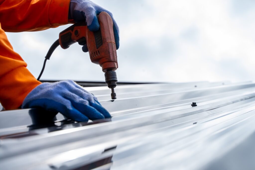 Close-up of a person using a power drill to fasten screws into a flat metal roof