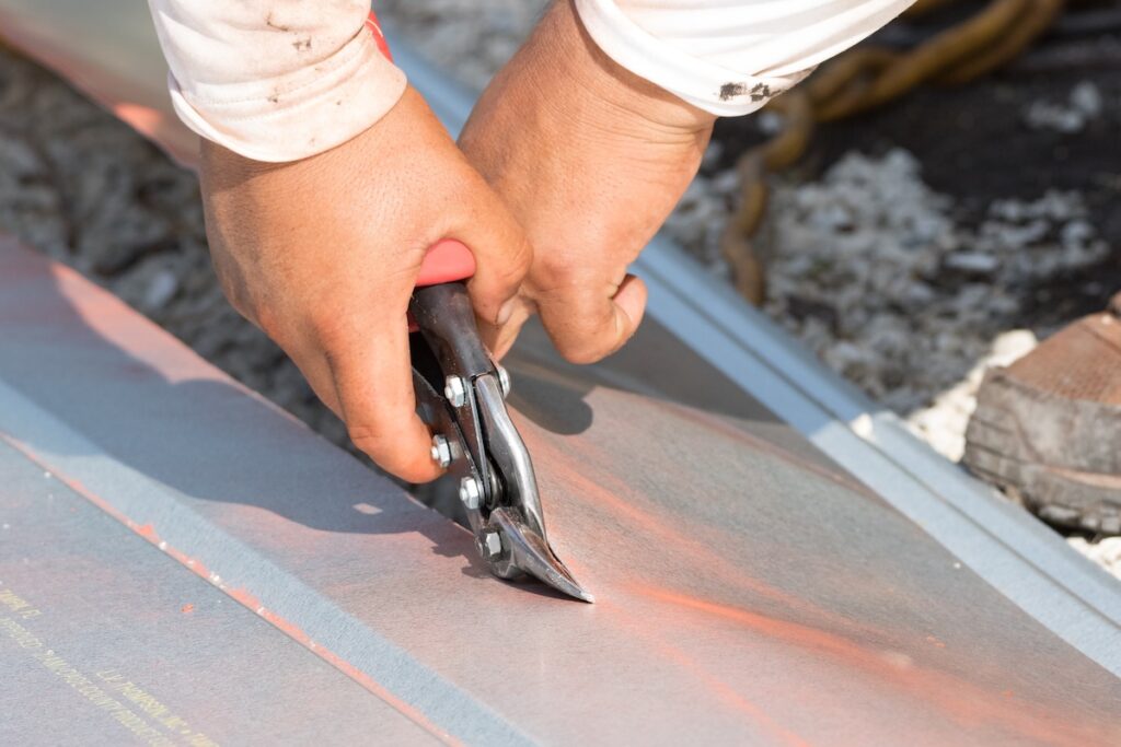 A person uses metal snips to cut a sheet of metal, holding the tool with both hands.