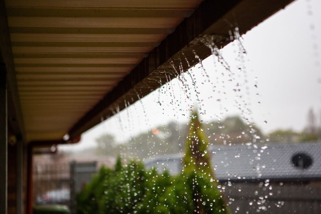 Rainwater pours off the edge of a roof, creating streams and droplets.