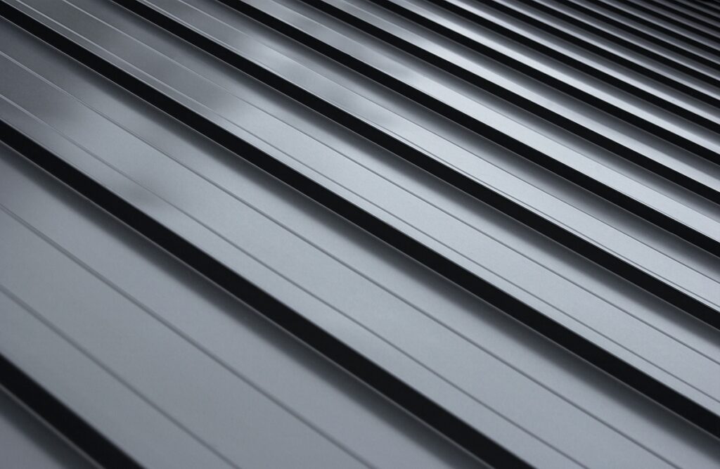 Close-up view of a dark gray standing seam metal roof with parallel ridges and grooves, creating a repeating linear pattern and a sense of depth and texture