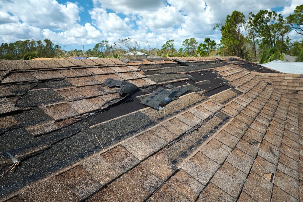 Damaged house roof with missing shingles after storm