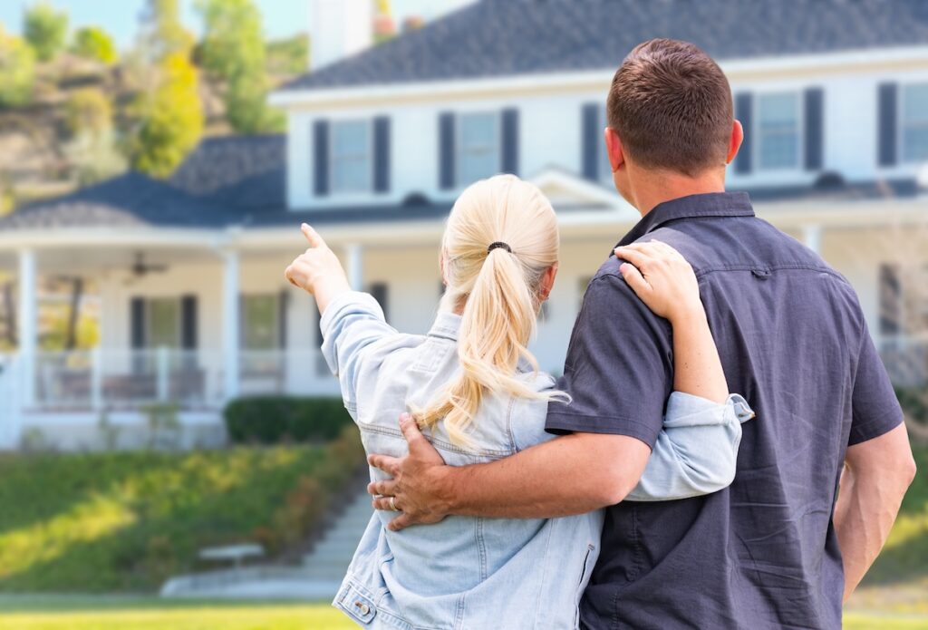 Young Adult Couple Facing and Pointing to Front of House.