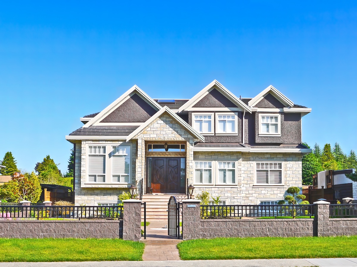A modern two-story house with gray stone exterior, white trim, large windows, and a dark front door, featuring expert roofing.